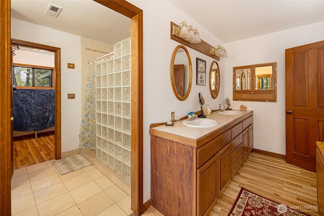 ensuite bathroom with visible vents, a sink, baseboards, and a tile shower
