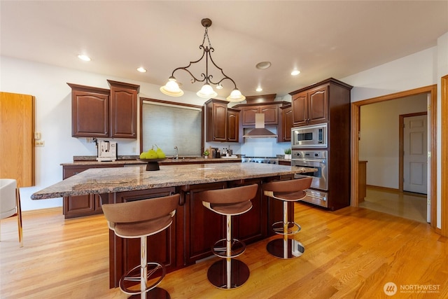 6714 89th Street Ct E, Puyallup, WA 98371 - kitchen with appliances with stainless steel finishes, a sink, a kitchen breakfast bar, a kitchen island, and light wood-style flooring