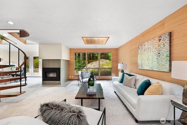 carpeted living room featuring a glass covered fireplace, plenty of natural light, and wood walls