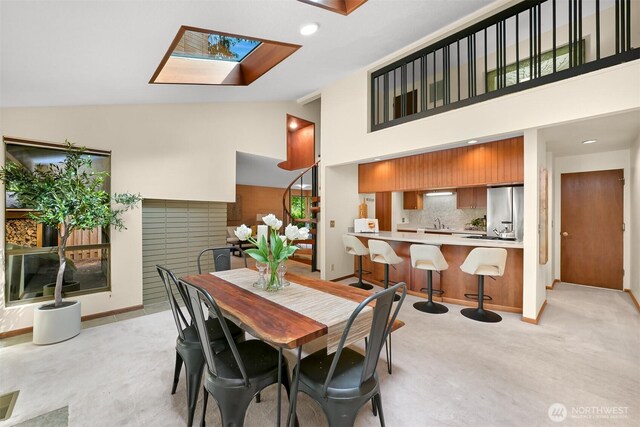 dining room featuring a skylight, baseboards, light carpet, and high vaulted ceiling