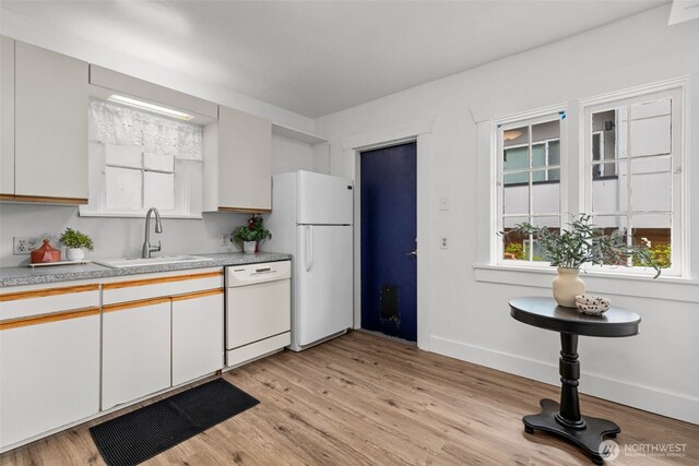 kitchen with a sink, light countertops, baseboards, light wood finished floors, and white appliances