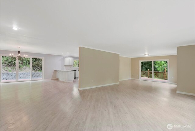 unfurnished living room featuring baseboards, ornamental molding, light wood-style flooring, and a chandelier