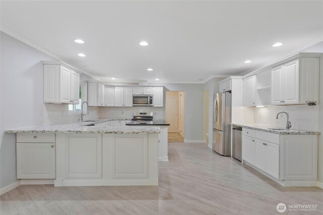 kitchen with a peninsula, baseboards, appliances with stainless steel finishes, and a sink