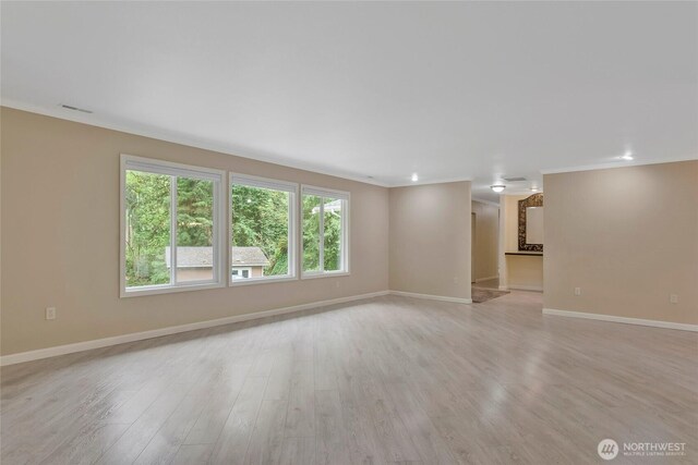 unfurnished living room featuring baseboards, light wood finished floors, crown molding, and visible vents