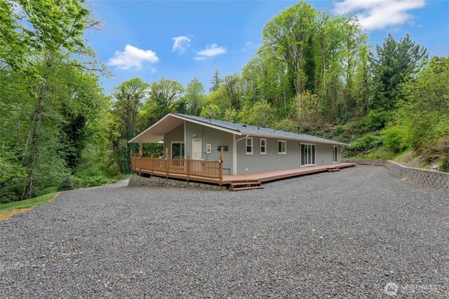 view of front of home with a wooded view, a wooden deck, and gravel driveway