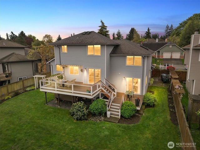 back of house at dusk featuring a fenced backyard, a shingled roof, a yard, and a deck