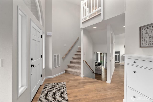 entrance foyer with visible vents, stairs, light wood-style floors, baseboards, and a high ceiling