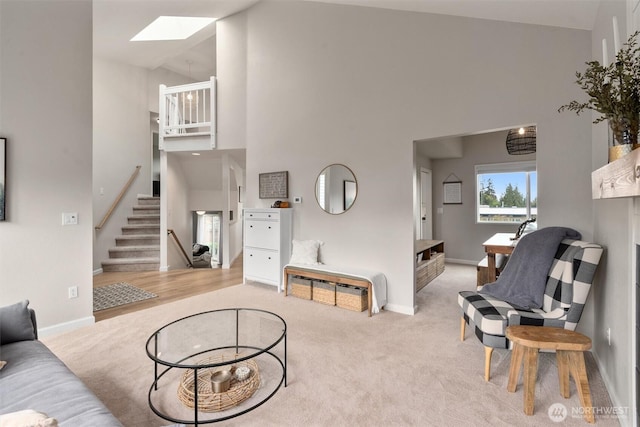 living area featuring a skylight, baseboards, carpet, and a towering ceiling