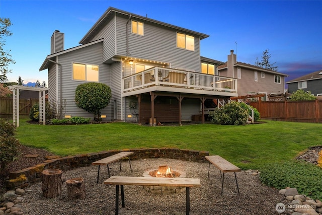 back of property with fence, a wooden deck, a lawn, and an outdoor fire pit