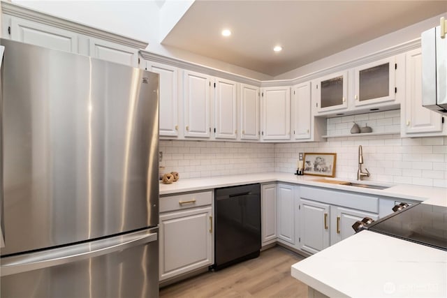 kitchen featuring a sink, dishwasher, light wood-style flooring, freestanding refrigerator, and backsplash