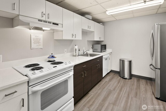 kitchen with appliances with stainless steel finishes, dark brown cabinets, a sink, light countertops, and under cabinet range hood