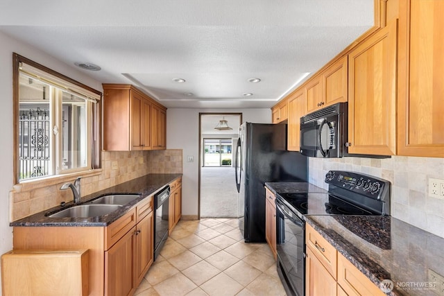 kitchen with decorative backsplash, a sink, light tile patterned floors, black appliances, and dark stone counters