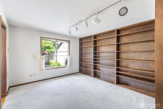 spare room featuring carpet floors, rail lighting, a textured ceiling, and baseboards