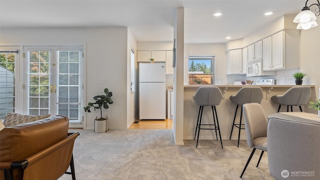 kitchen featuring a breakfast bar, light carpet, white appliances, and a healthy amount of sunlight