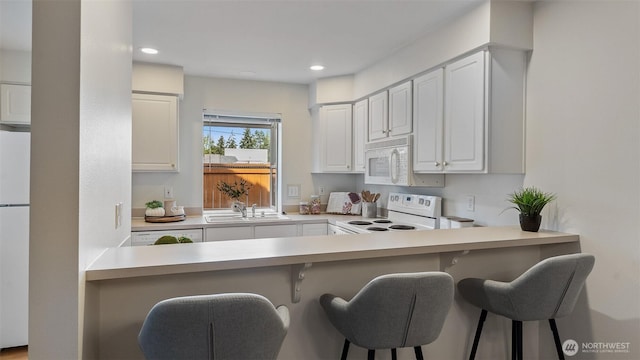 kitchen featuring a sink, recessed lighting, a kitchen bar, and white appliances