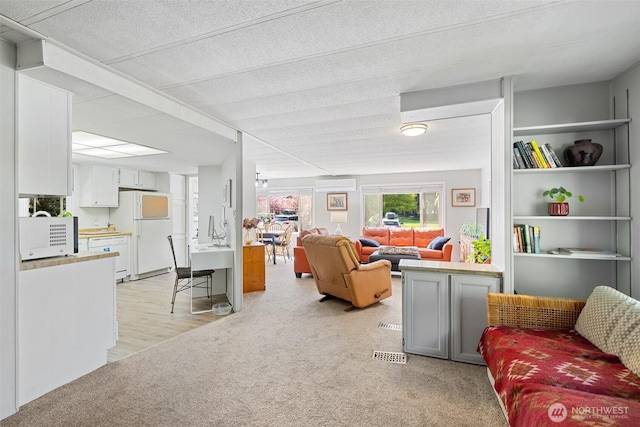 living area featuring visible vents, a wall mounted air conditioner, and light carpet
