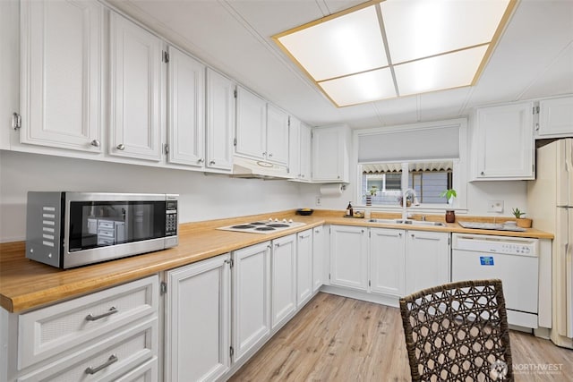 kitchen featuring white appliances, light countertops, under cabinet range hood, white cabinets, and a sink