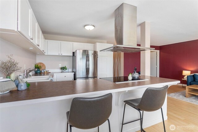 kitchen featuring island range hood, a sink, freestanding refrigerator, light wood finished floors, and black electric stovetop