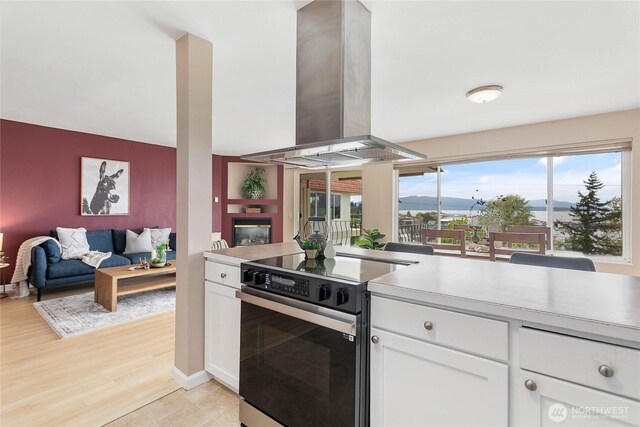 kitchen featuring range with electric stovetop, island exhaust hood, light countertops, white cabinets, and open floor plan