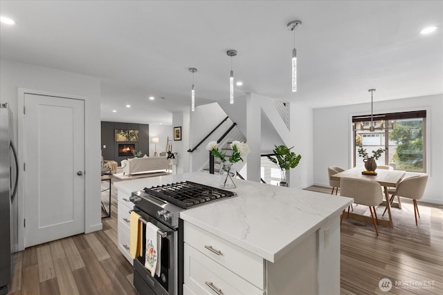 kitchen with pendant lighting, appliances with stainless steel finishes, wood finished floors, open floor plan, and white cabinetry