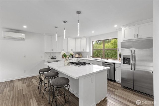 kitchen featuring a sink, light countertops, an AC wall unit, a center island, and stainless steel appliances