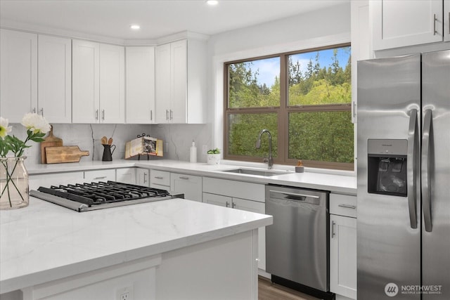 kitchen with appliances with stainless steel finishes, a sink, light stone counters, recessed lighting, and white cabinetry