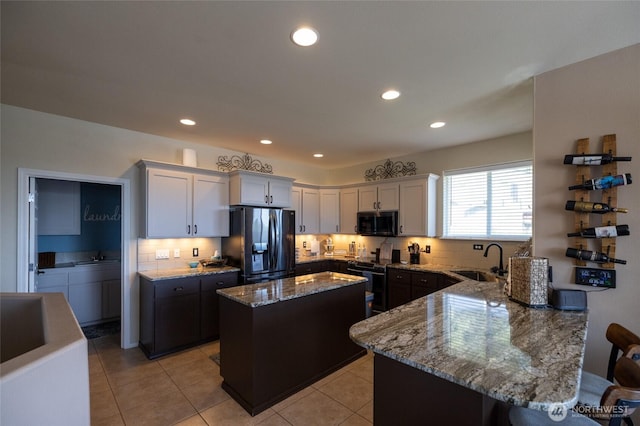 kitchen with light stone countertops, a sink, black appliances, and tasteful backsplash