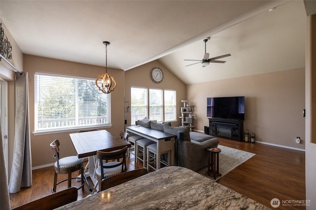 interior space featuring baseboards, ceiling fan with notable chandelier, wood finished floors, and lofted ceiling