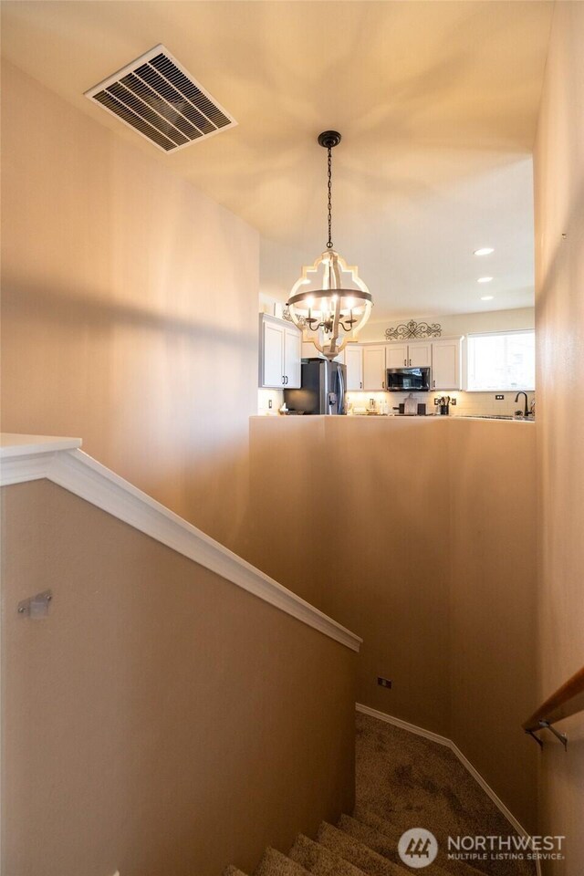 stairs featuring visible vents, baseboards, carpet floors, and a notable chandelier