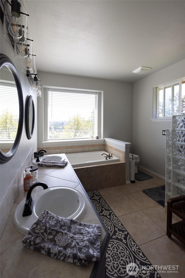 bathroom with a sink, tile patterned flooring, a garden tub, and toilet