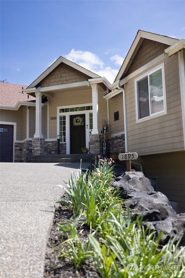 craftsman inspired home with covered porch, stone siding, and a garage