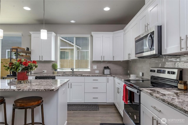 kitchen with white cabinets, appliances with stainless steel finishes, a sink, decorative backsplash, and wood finished floors