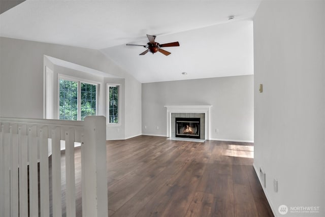 unfurnished living room featuring ceiling fan, lofted ceiling, dark wood-style flooring, a tiled fireplace, and baseboards