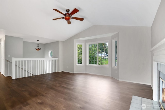 unfurnished living room with wood finished floors, a ceiling fan, lofted ceiling, a tiled fireplace, and baseboards