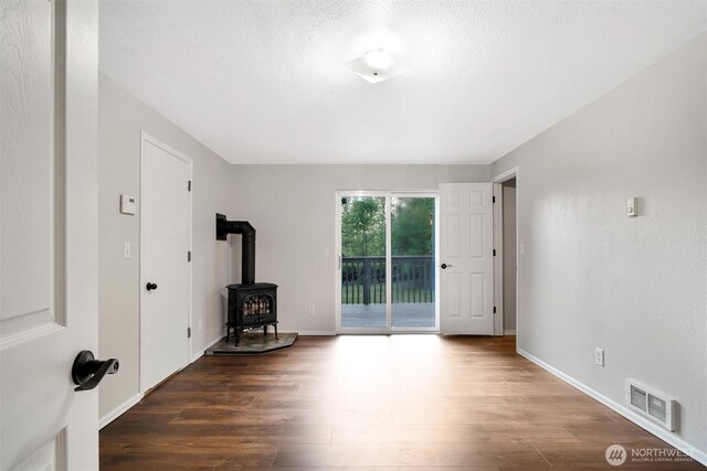 unfurnished room with a wood stove, wood finished floors, and baseboards