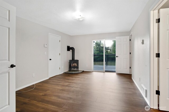 unfurnished room with a wood stove, wood finished floors, and baseboards