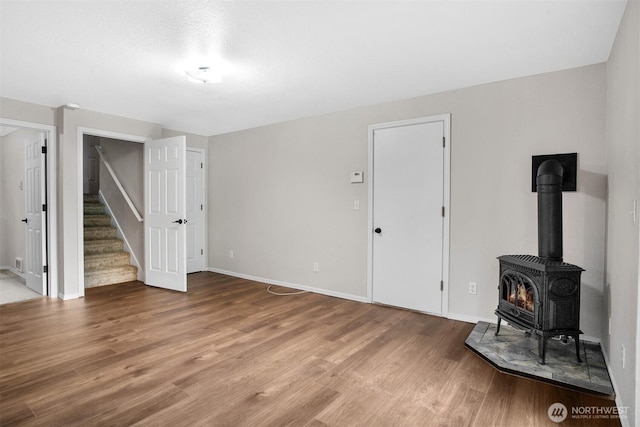 unfurnished living room with wood finished floors, baseboards, stairway, and a wood stove