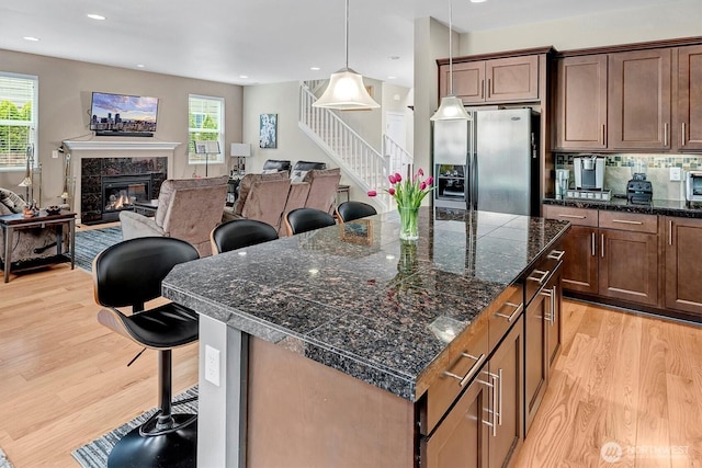 kitchen featuring a kitchen breakfast bar, a healthy amount of sunlight, stainless steel fridge with ice dispenser, and light wood-type flooring