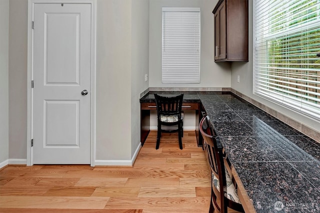 unfurnished office with baseboards, light wood-type flooring, and built in desk
