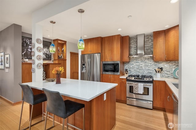 kitchen featuring wall chimney range hood, appliances with stainless steel finishes, brown cabinetry, and light wood finished floors