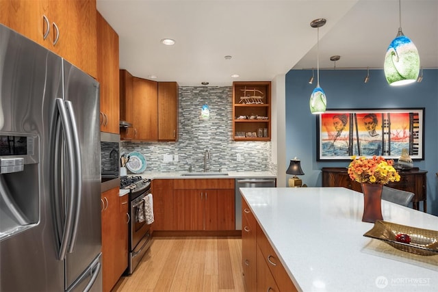 kitchen featuring brown cabinets, appliances with stainless steel finishes, a sink, light wood-style floors, and light countertops