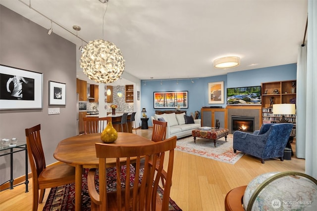 dining space featuring light wood-style floors, a notable chandelier, and a warm lit fireplace