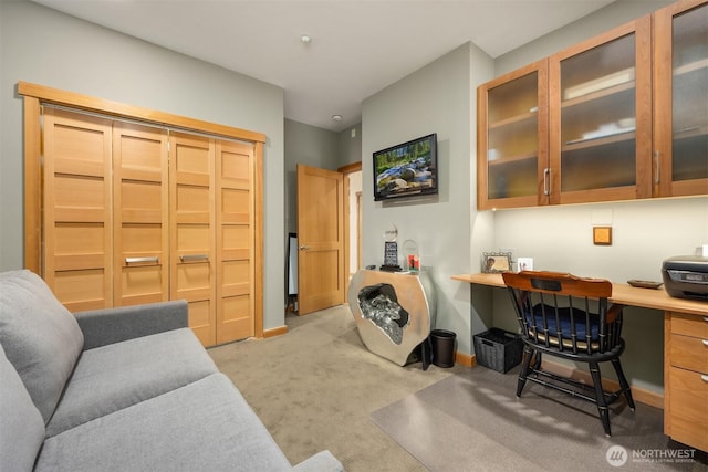 home office with built in study area, baseboards, and light carpet