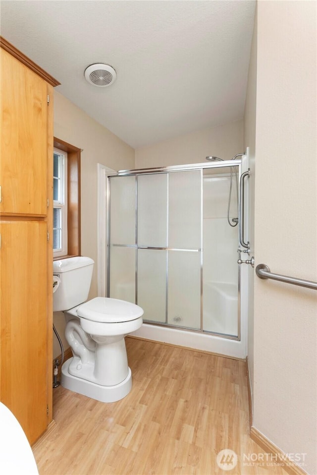 full bath with a shower stall, toilet, and wood finished floors