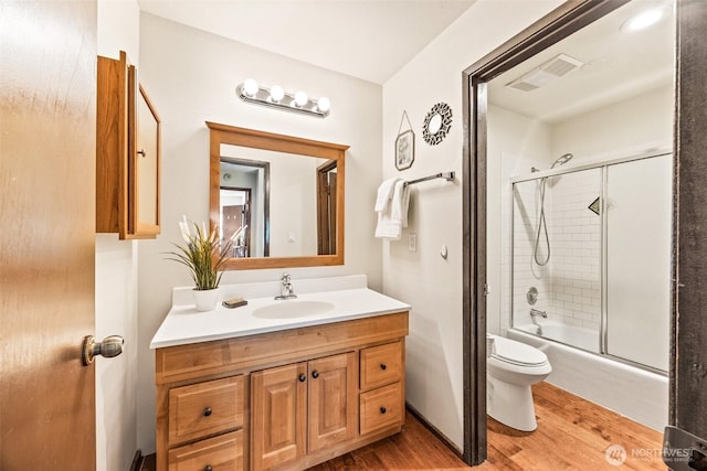 full bath featuring wood finished floors, toilet, vanity, and combined bath / shower with glass door