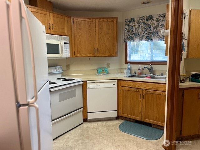 kitchen featuring a sink, light countertops, brown cabinetry, and white appliances