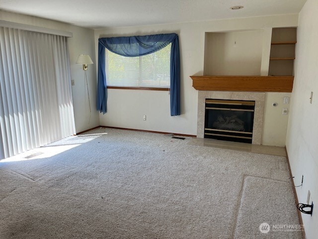 unfurnished living room with a tiled fireplace, carpet, and visible vents