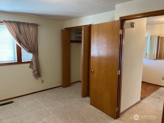 unfurnished bedroom featuring light colored carpet, a textured ceiling, baseboards, visible vents, and a closet