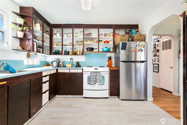 kitchen with freestanding refrigerator, white range with gas cooktop, open shelves, and arched walkways
