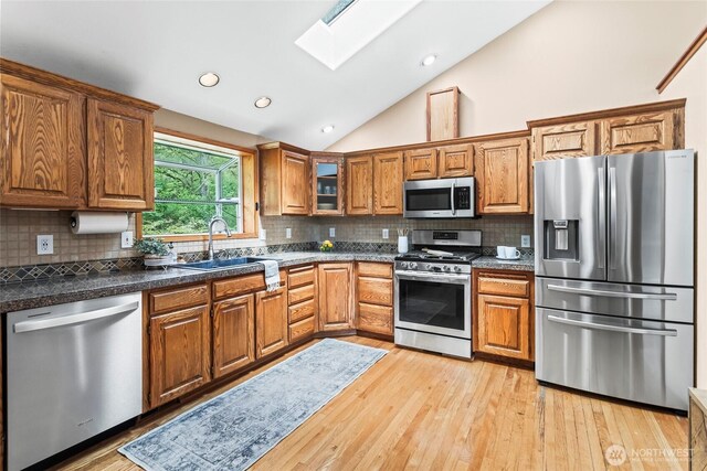 kitchen featuring vaulted ceiling with skylight, tasteful backsplash, brown cabinets, light wood-style floors, and stainless steel appliances